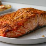 Close-up of a beautifully seasoned and cooked air fryer salmon fillet resting on a white plate.