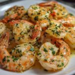 Close-up of juicy, seasoned air fryer shrimp coated in melted butter, garlic, and fresh parsley on a white plate.