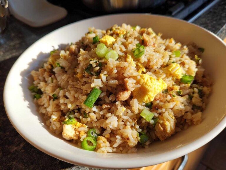 A close-up of a white bowl filled with savory chicken fried rice, featuring scrambled egg and green onions.