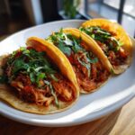 Three golden corn tortillas filled with shredded, saucy chicken filling and topped generously with fresh cilantro for amazing chicken tacos.