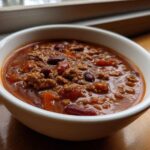 Close-up of a white bowl filled with rich, thick crockpot chili featuring ground meat and kidney beans.
