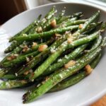 Close-up of bright green beans roasted with crispy garlic bits in a white bowl.