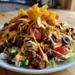 A vibrant, close-up view of a hearty taco salad piled high with seasoned beef, lettuce, tomatoes, olives, and dressing.