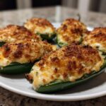 A plate of six baked jalapeño poppers stuffed with creamy filling and topped with crispy breadcrumbs.