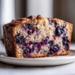 A close-up slice of moist blueberry banana bread showing abundant blueberries in the crumb.