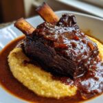A close-up of tender braised short ribs smothered in rich sauce, served over creamy polenta.