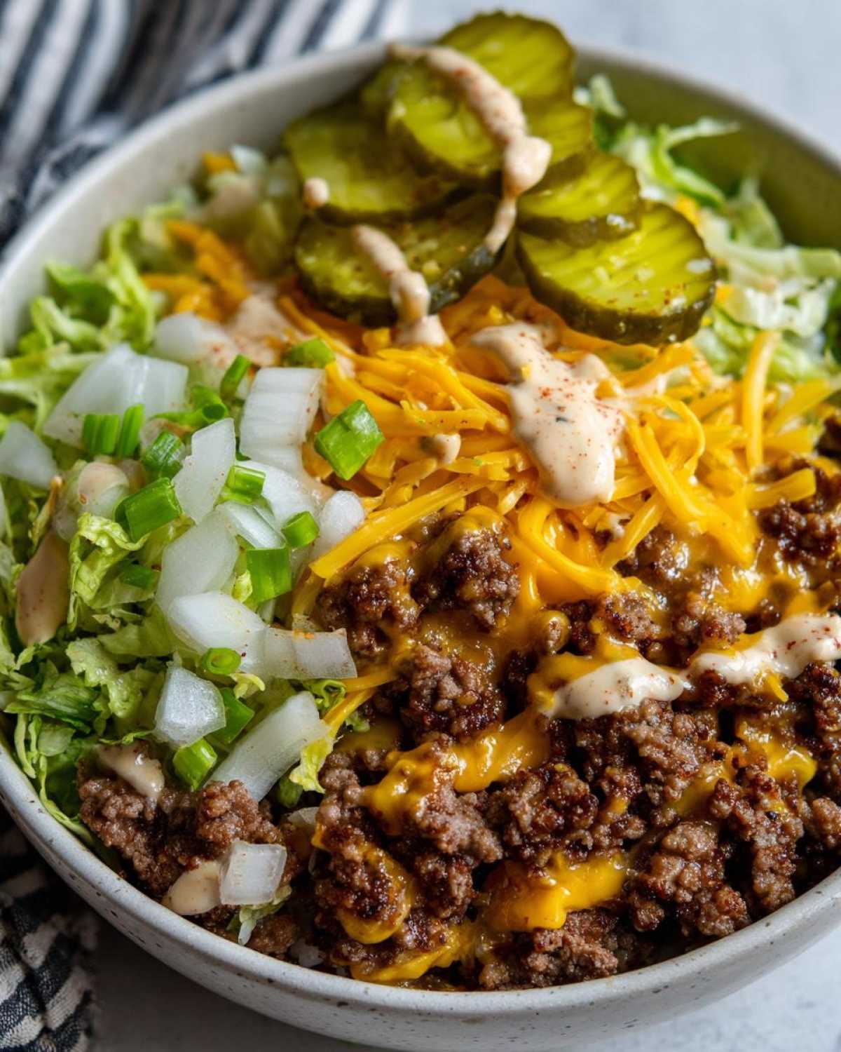 Close-up of a delicious cheeseburger bowl featuring ground beef, melted cheese, lettuce, onions, pickles, and special sauce.