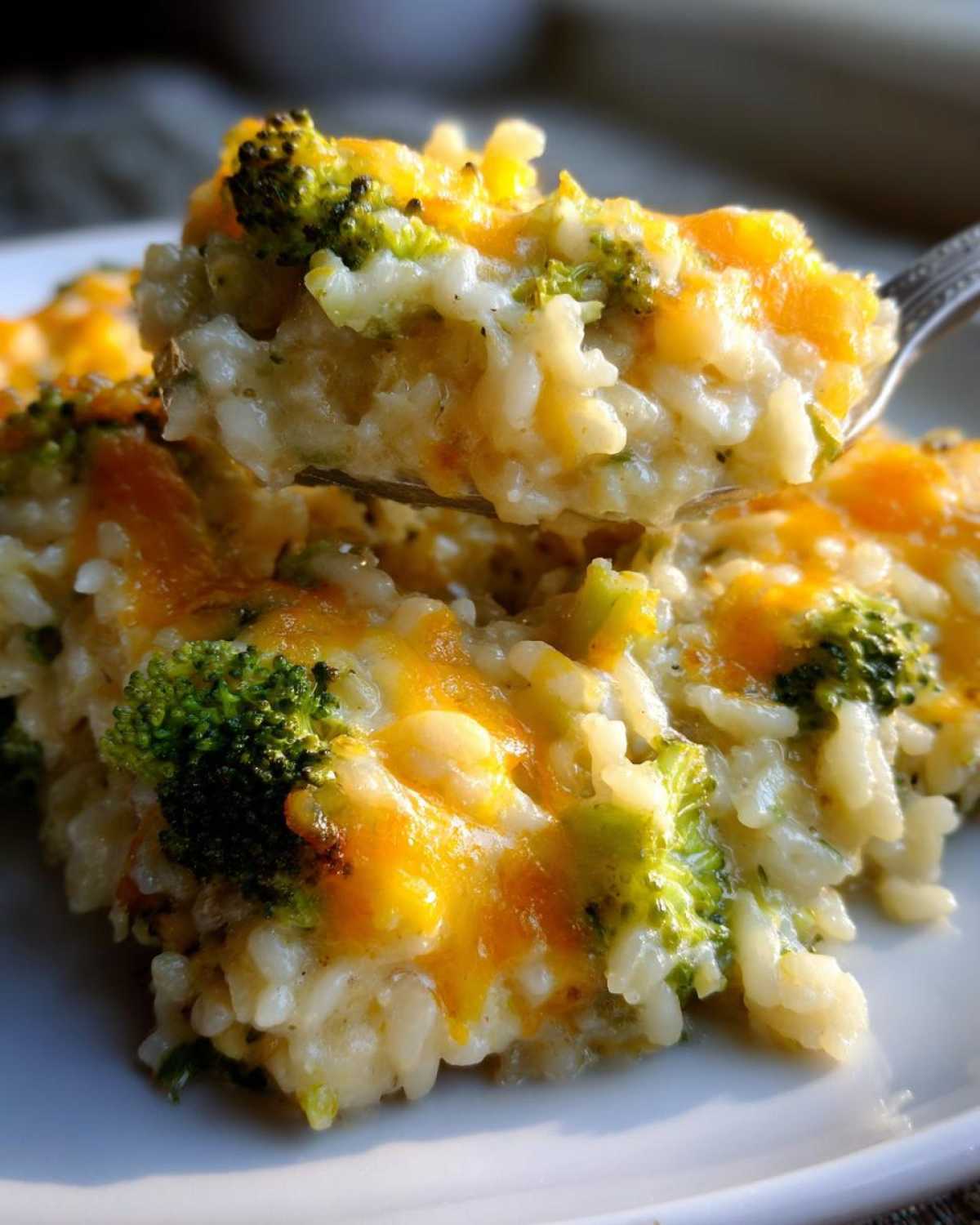 A spoonful of creamy, cheesy broccoli rice being lifted from a white plate.