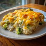A close-up serving of cheesy chicken and rice mixed with bright green broccoli florets, topped with melted cheddar cheese.