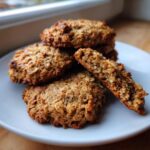 A stack of golden brown, textured breakfast cookie treats on a white plate, one broken open to show the interior.