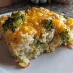 A close-up of a serving of creamy chicken broccoli rice casserole topped with melted cheddar cheese.