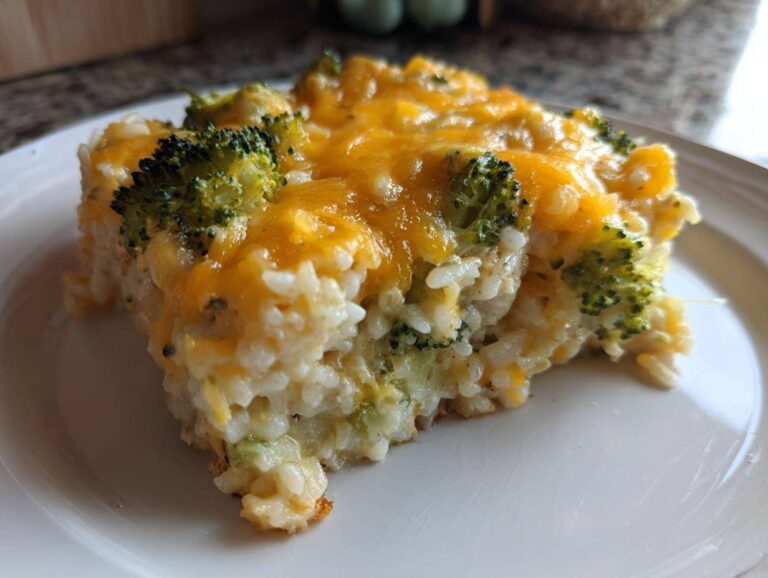 A close-up of a serving of creamy chicken broccoli rice casserole topped with melted cheddar cheese.