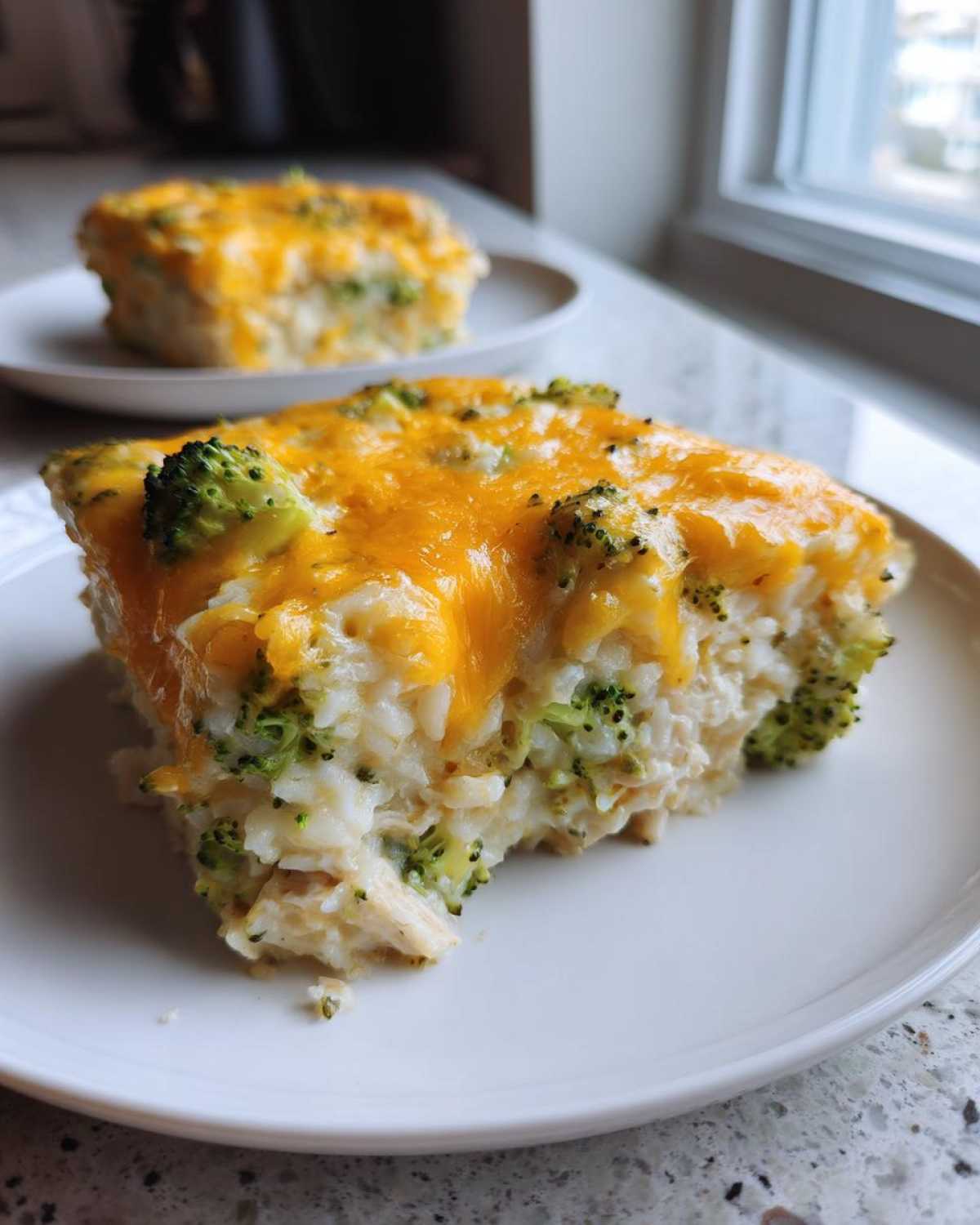 Close-up of a serving of creamy chicken broccoli rice casserole topped with melted cheddar cheese.