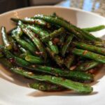 Close-up of vibrant chinese green beans with garlic sauce served in a white bowl.