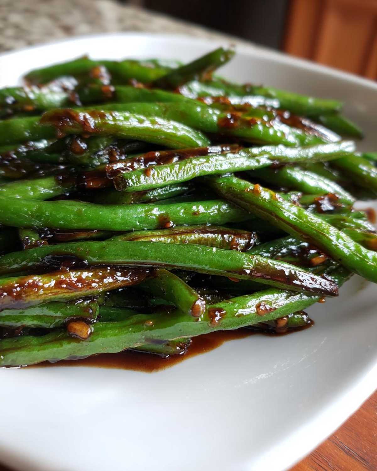 A close-up of bright green, glossy chinese green beans with garlic sauce piled on a white plate.