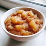 A close-up of chunky, homemade applesauce sprinkled with cinnamon served in a small white bowl.