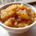 Close-up of chunky homemade applesauce in a white bowl, sprinkled with cinnamon.
