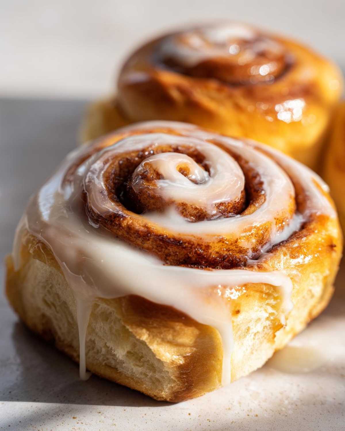 A close-up of a freshly baked cinnamon roll topped with thick, dripping white icing.