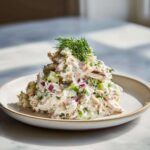 A mound of creamy cottage cheese chicken salad mixed with celery and red onion, topped with fresh dill.