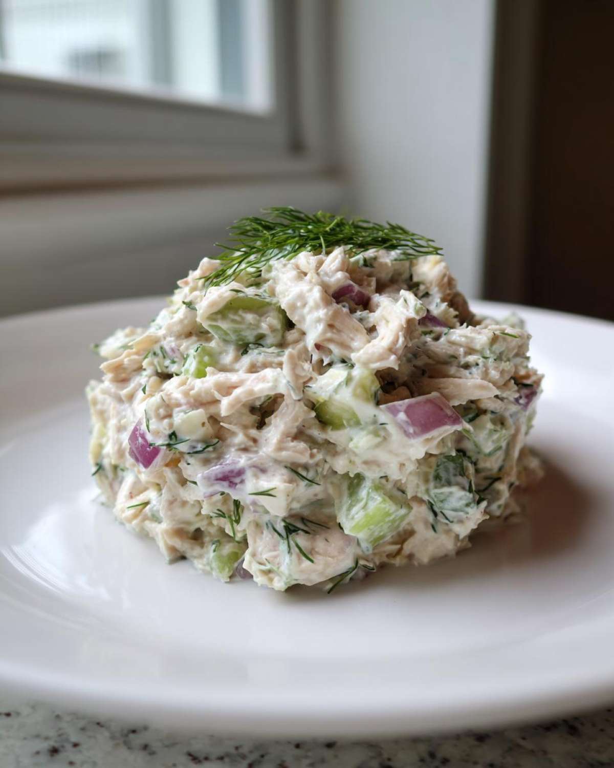 A scoop of creamy cottage cheese chicken salad mixed with celery and red onion, topped with fresh dill.