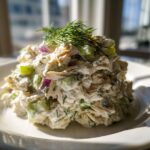 A mound of creamy cottage cheese chicken salad mixed with celery and red onion, topped with fresh dill.