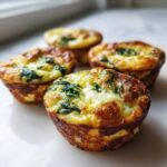 Four golden brown cottage cheese egg cups with visible spinach baked in, resembling Starbucks egg bites.