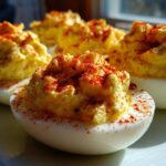 Close-up of creamy deviled eggs piped high and dusted generously with bright red paprika.