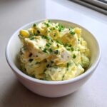 A white bowl filled with creamy egg salad recipe, garnished generously with chopped green chives.