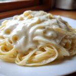 Close-up of fettuccine pasta generously coated in thick, creamy homemade alfredo sauce.
