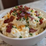 Close-up of a bowl of creamy Million Dollar Dip topped generously with crispy bacon bits and fresh green chives.
