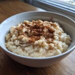 A close-up of a bowl of creamy rice pudding generously dusted with cinnamon.
