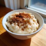 A close-up of creamy rice pudding served in a white bowl, generously dusted with cinnamon.
