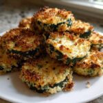 A pile of crispy, golden-brown baked parmesan zucchini rounds stacked on a white plate.