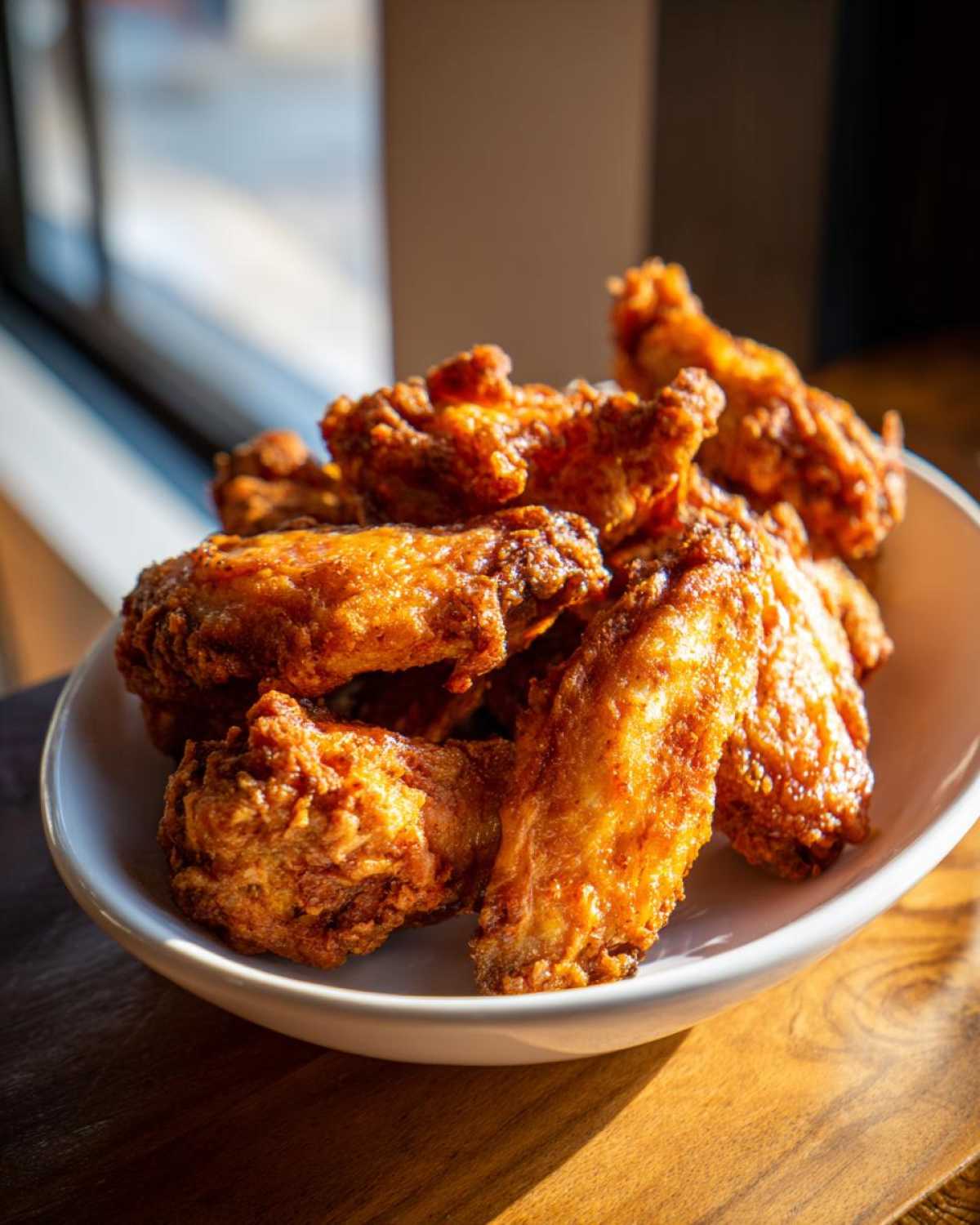 A close-up shot of perfectly crispy, golden brown chicken wings piled high in a white bowl.