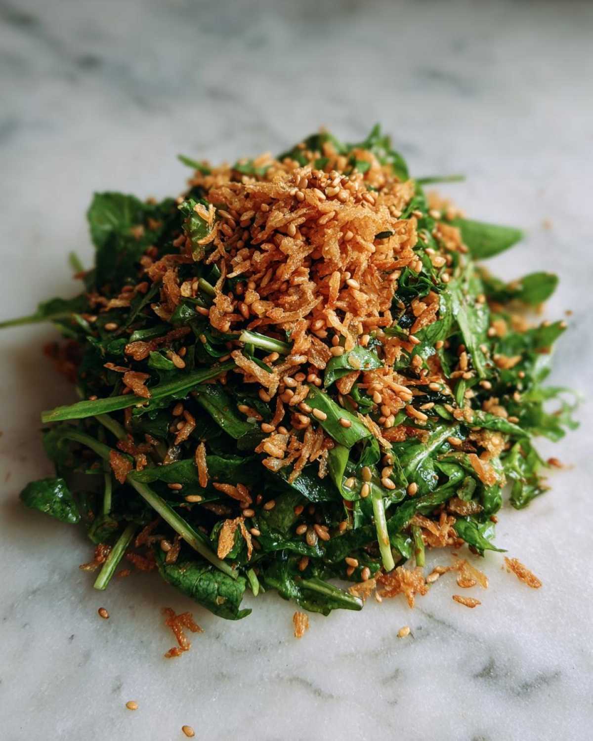 A mound of fresh greens topped generously with golden brown crispy rice pieces and sesame seeds, characteristic of a crispy rice salad.
