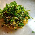 Close-up of a single, formed portion of crispy rice salad topped generously with fresh green herbs and sesame seeds.