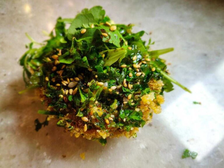 Close-up of a single, formed portion of crispy rice salad topped generously with fresh green herbs and sesame seeds.