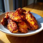 Close-up of perfectly crispy, golden-brown seasoned chicken wings piled on a white plate.