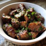 Close-up of tender, browned crockpot steak bites coated in a savory sauce and topped with fresh chopped parsley.