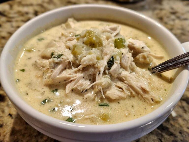 A close-up view of a hearty bowl of creamy crockpot white chicken chili, topped with shredded chicken and green chiles.