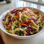 A vibrant bowl filled with crunchy cabbage salad featuring shredded green cabbage, red cabbage, and bright orange carrots.