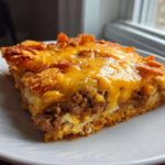 A square slice of Dorito Casserole topped with melted cheddar cheese and crunchy Doritos pieces.