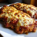 Close-up of two golden-brown pieces of Easy Chicken Parmesan topped with bubbling marinara sauce and melted mozzarella cheese.