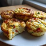 A plate holding several golden brown Egg Muffin Cups, one of which has a bite taken out showing the fluffy interior.