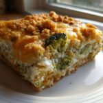 A close-up of a square slice of creamy broccoli casserole topped with melted cheese and golden crumbs.