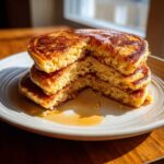 Close-up of a fluffy stack of almond flour pancakes with a bite taken out, drizzled with maple syrup.