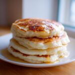 A tempting stack of four fluffy almond flour pancakes drizzled generously with golden syrup.