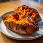 Two halves of a fluffy baked sweet potato with bright orange flesh served on a light gray plate.