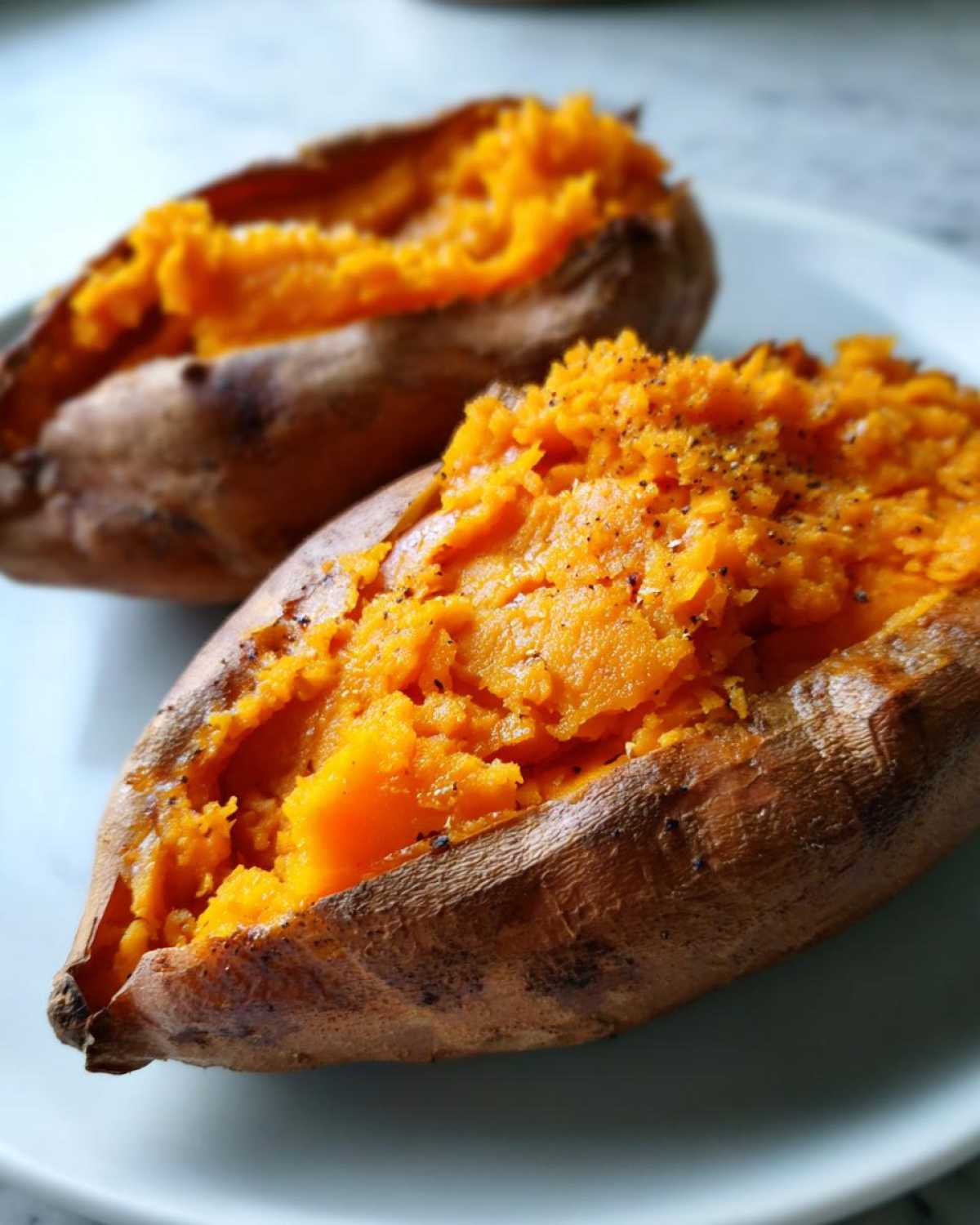 Close-up of two fluffy baked sweet potato halves, seasoned with black pepper, ready to eat.