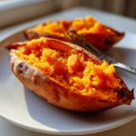 Close-up of fluffy baked sweet potatoes, split open to show bright orange interior on a white plate.